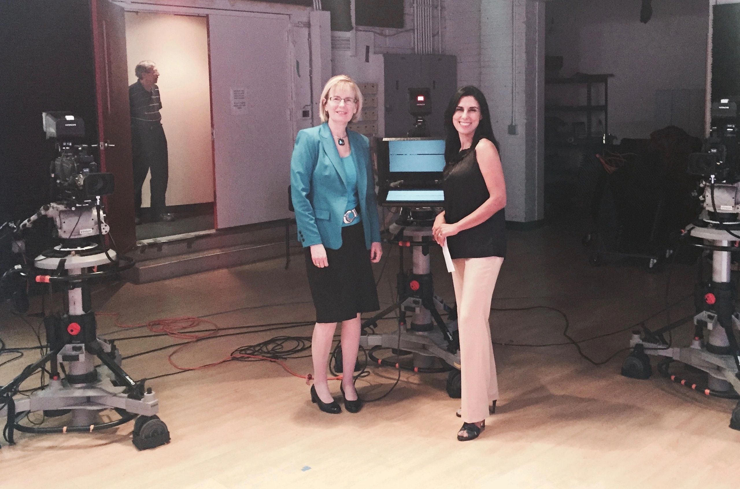 Two women standing in a TV studio surrounded by cameras and equipment